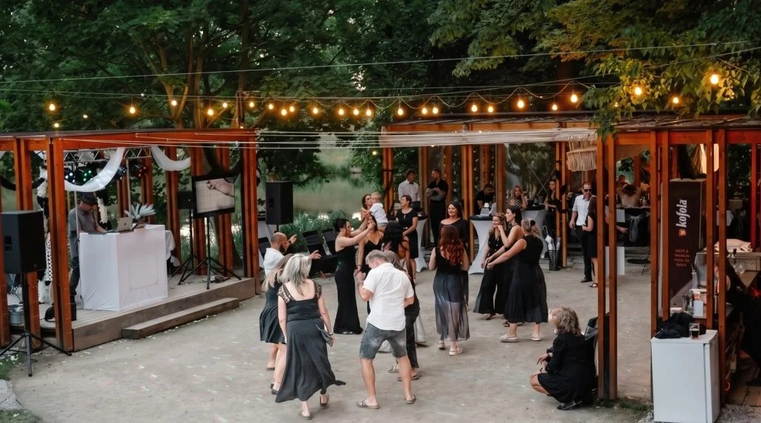Svatební hosté tančí na venkovním parketu pod světelnými řetězy, vedle je DJ pult a ozvučení.